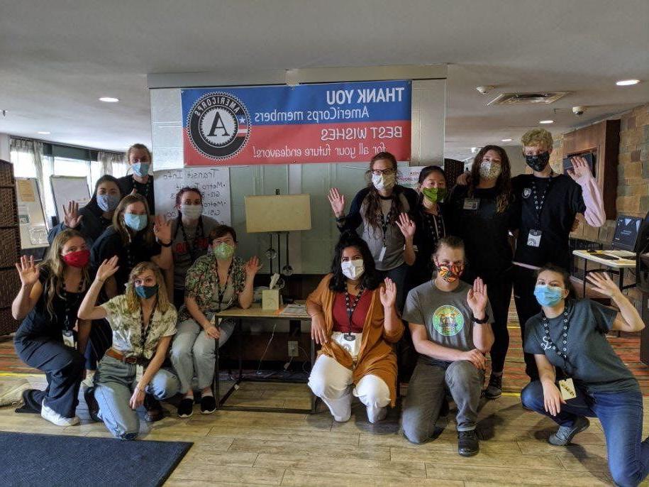 A group of people standing and kneeling around a sign thanking AmeriCorps members